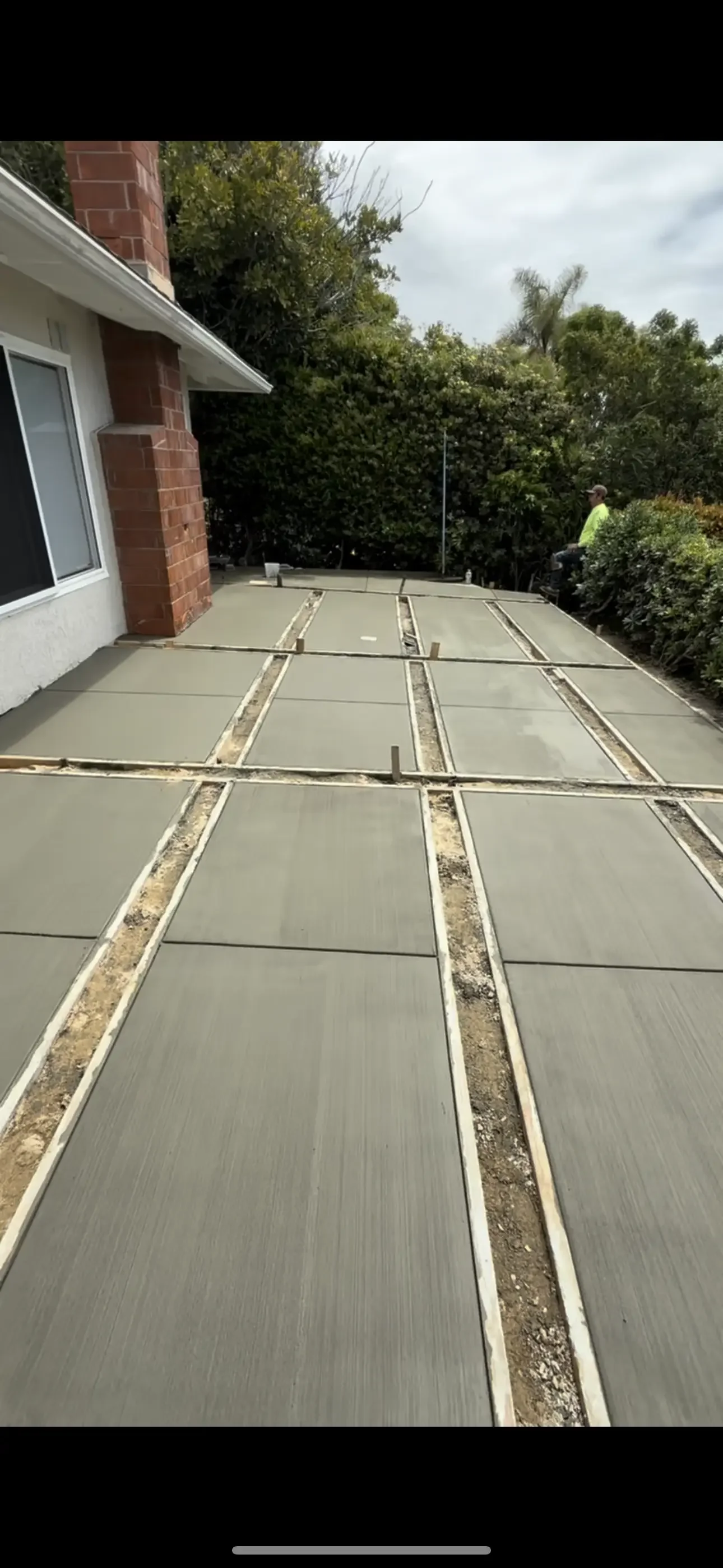 Freshly poured concrete patio slabs with wood forms and broom finish beside a stucco and brick house wall