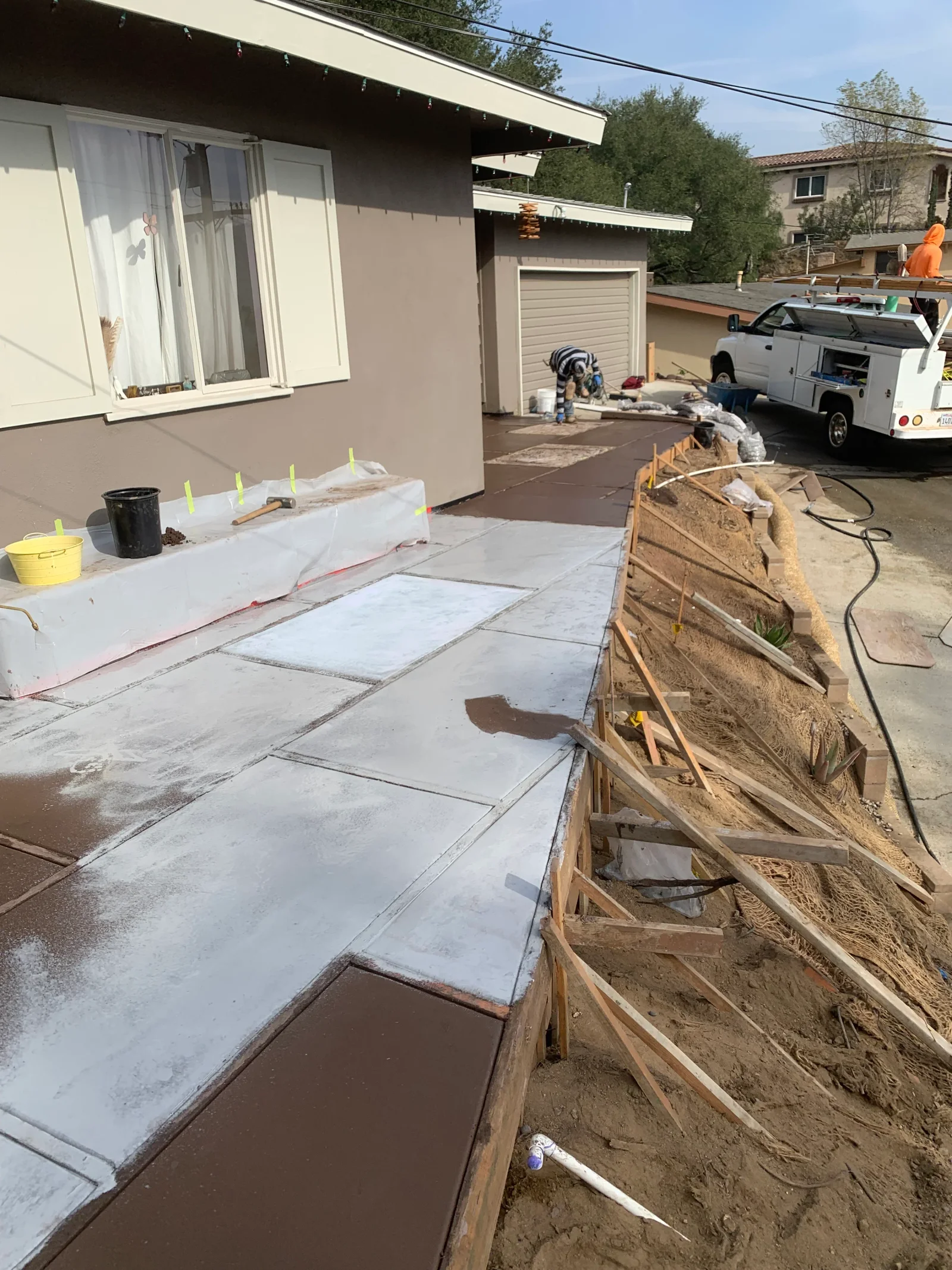 Concrete patio with scored panels and light gray overlay, wood form edging, and erosion control fabric on slope