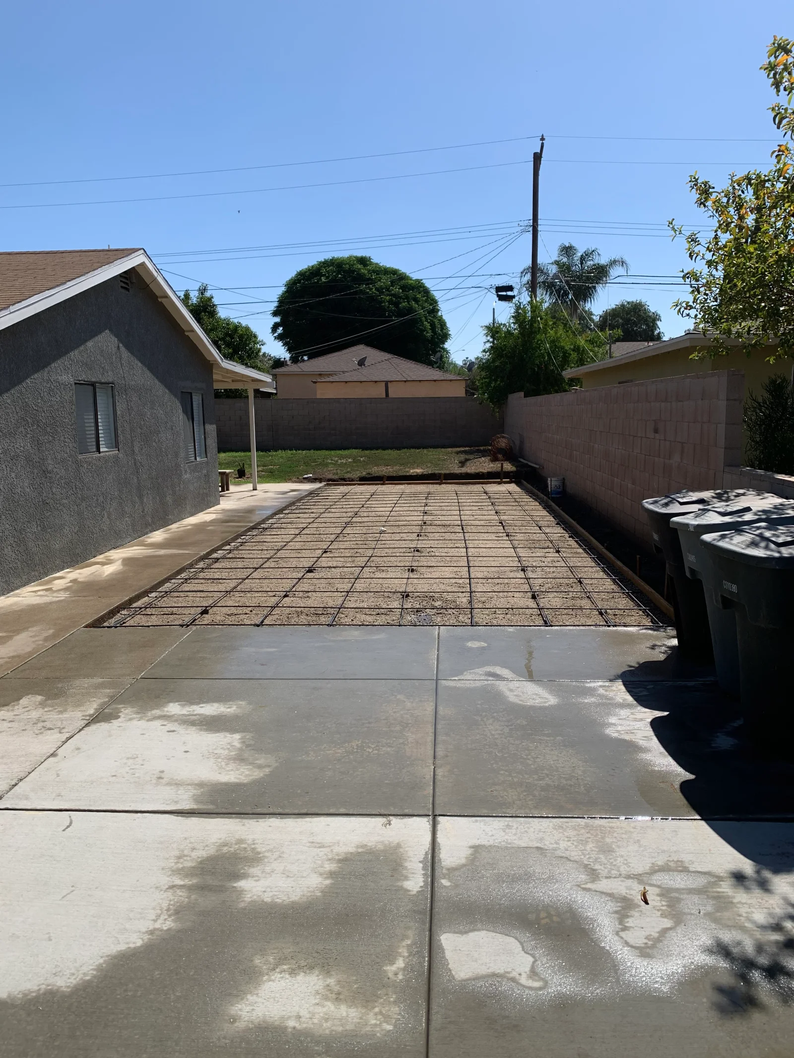 Rebar grid over compacted gravel base with wood forms, adjacent to freshly finished concrete patio