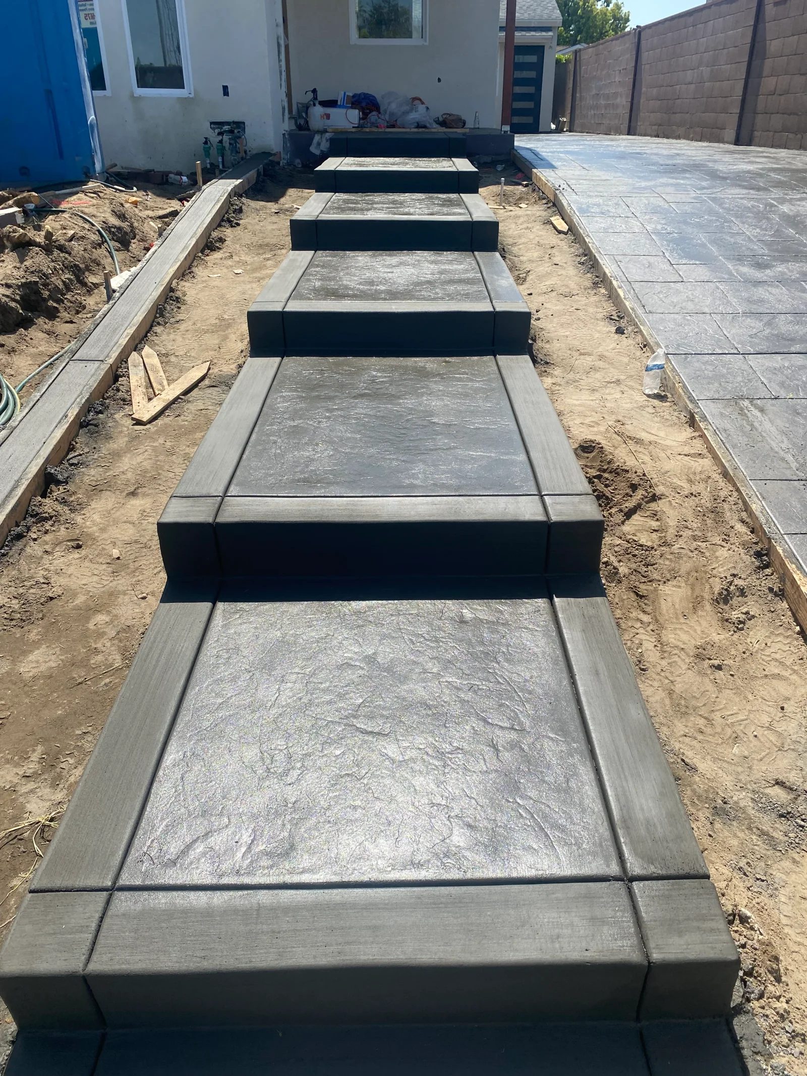 Dark gray stamped concrete stairway with smooth-finished risers and sidewalls, slate-pattern stamped concrete beside it