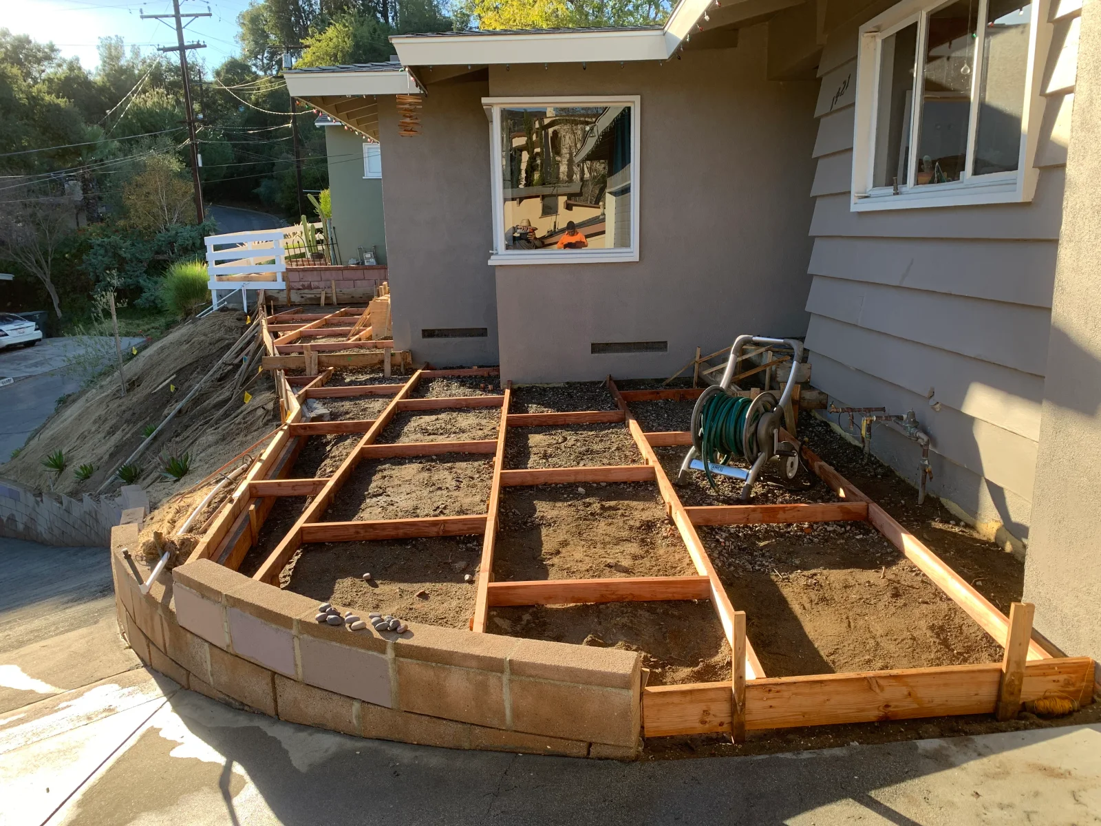 Redwood forms and grade beams set for concrete slab beside curved concrete block retaining wall