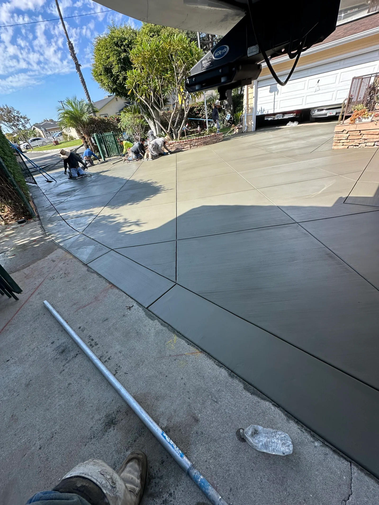 Crew finishing a freshly poured concrete driveway with trowels and saw-cut control joints in a geometric layout