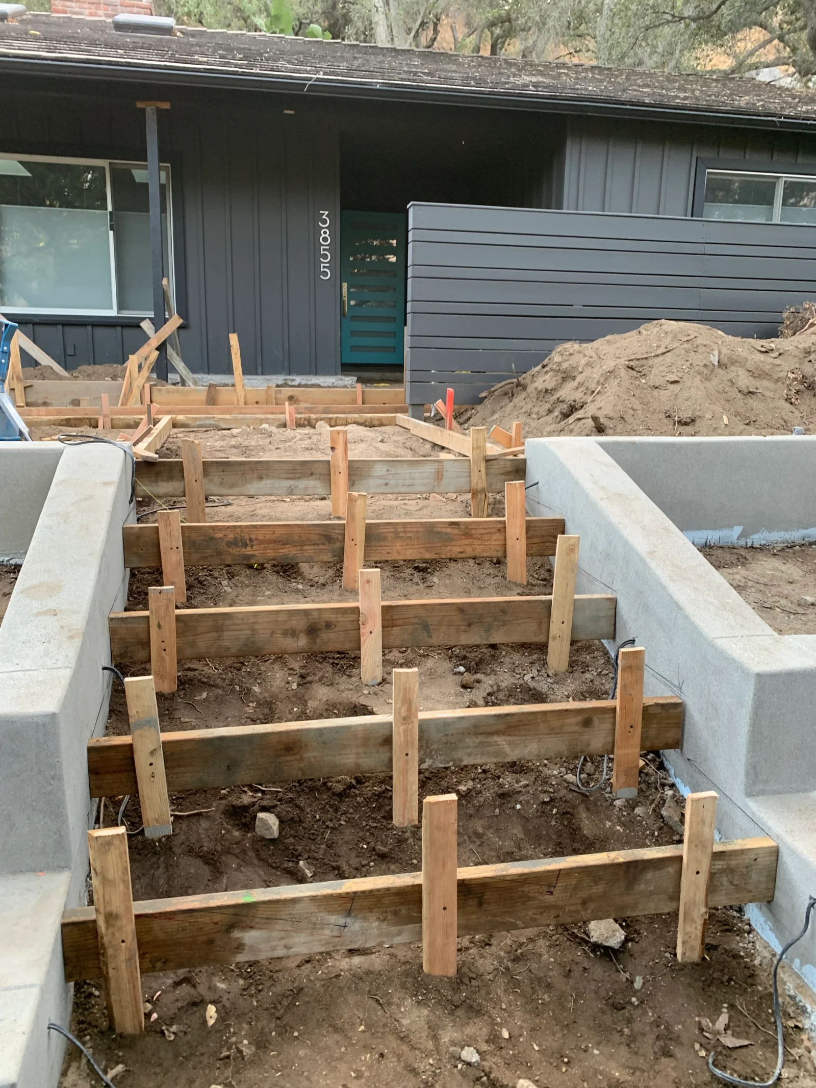Wood form boards and stakes set for stepped concrete footings beside poured concrete walls
