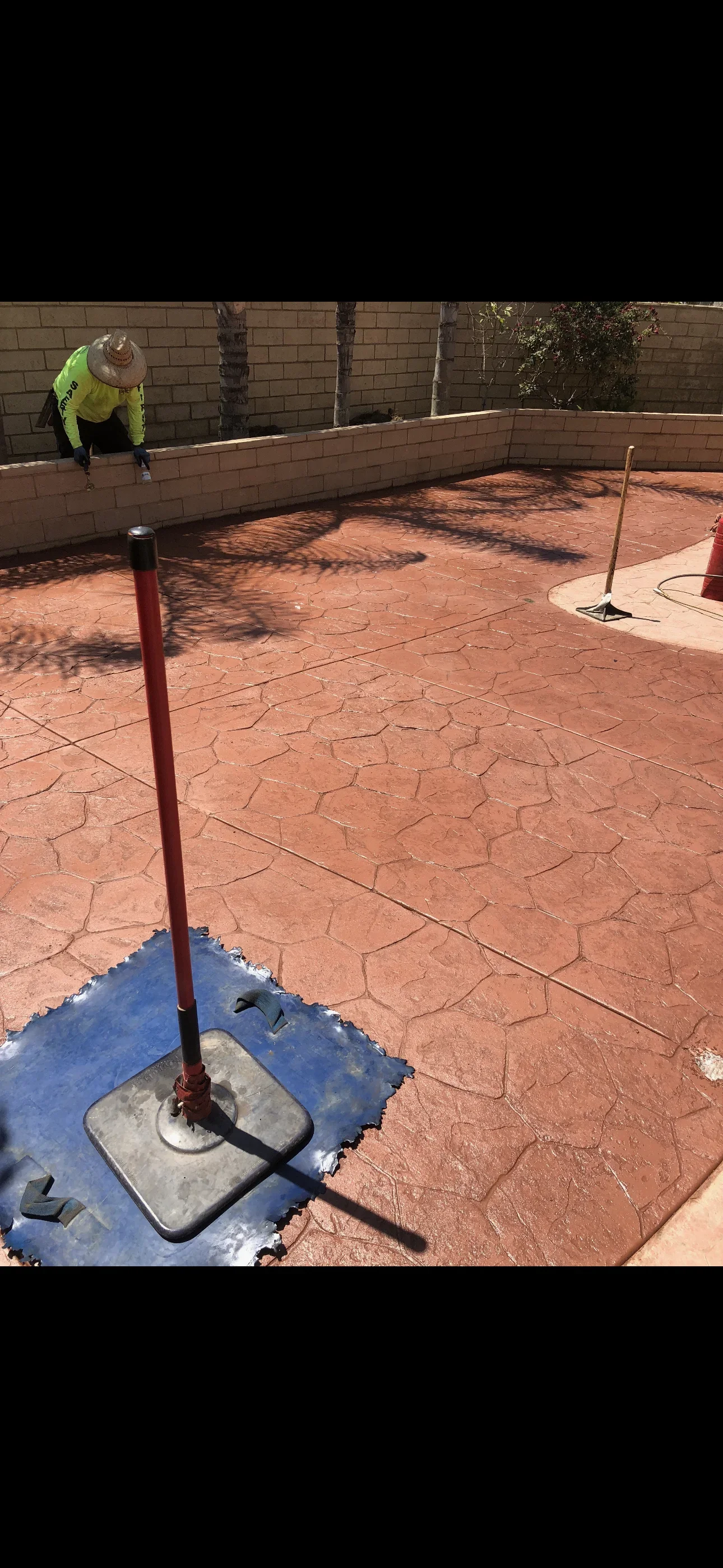Red stamped concrete patio with irregular flagstone pattern, curved border, and block wall with control joints