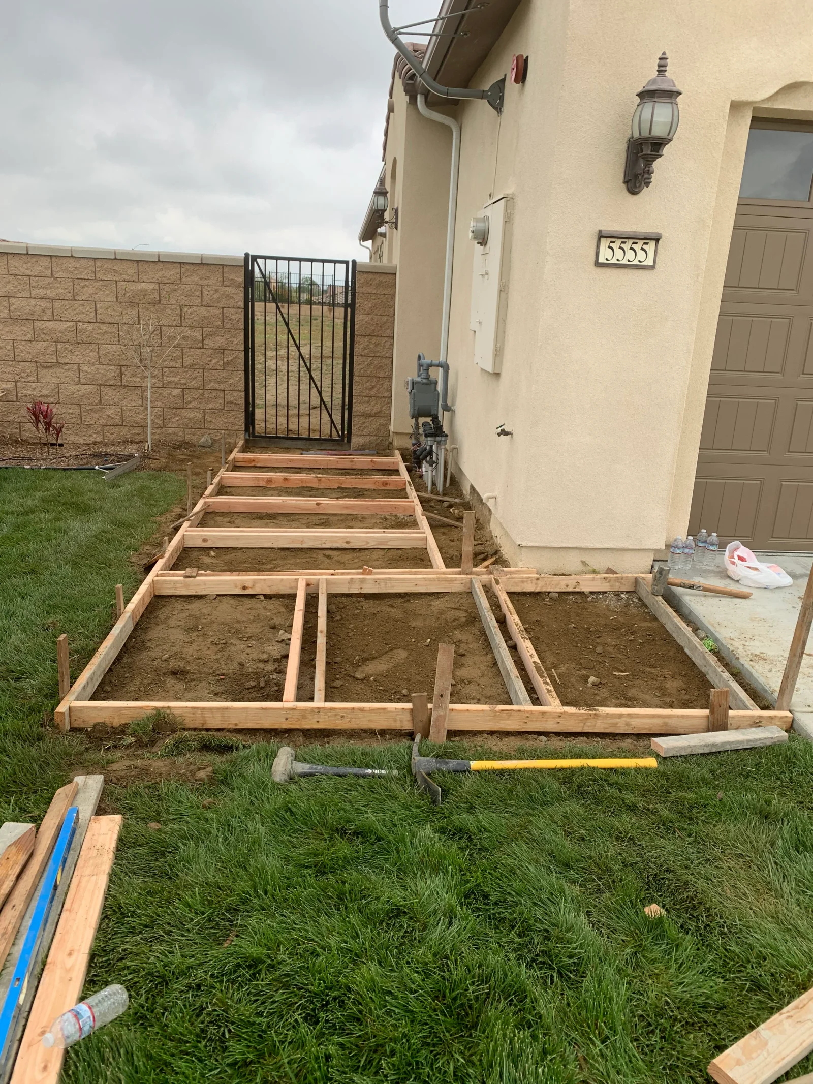 Wood lumber concrete slab forms staked into dirt with interior divider boards beside a stucco house