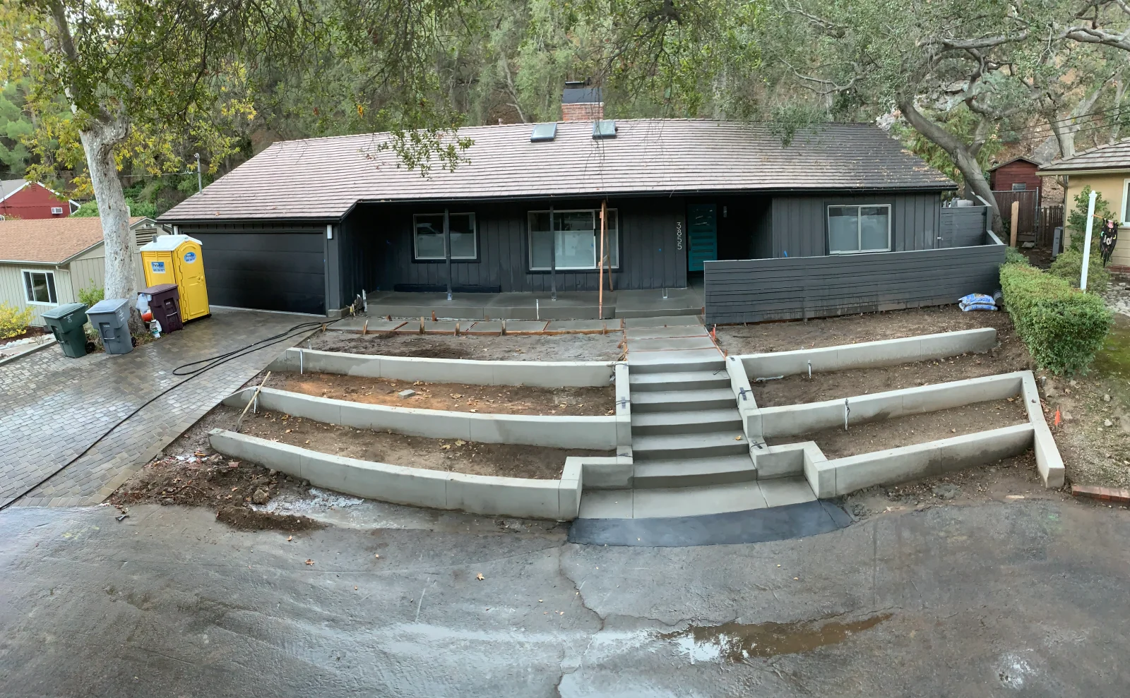 Curved tiered concrete retaining walls and center concrete staircase under construction at a front entry with fresh concrete porch slab