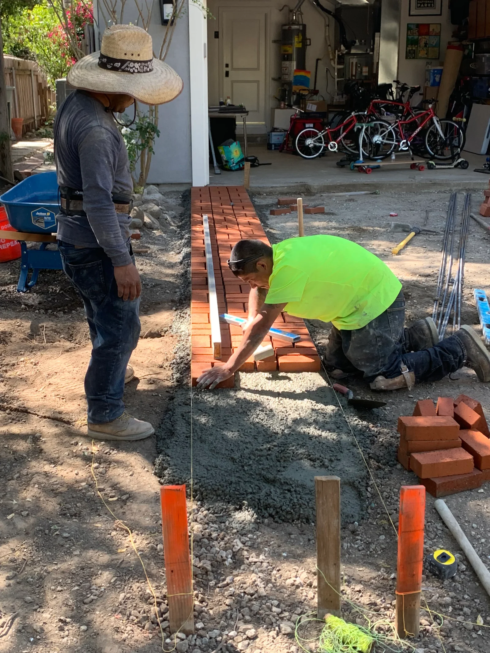 Worker setting red clay bricks in mortar bed with level and string line for walkway installation