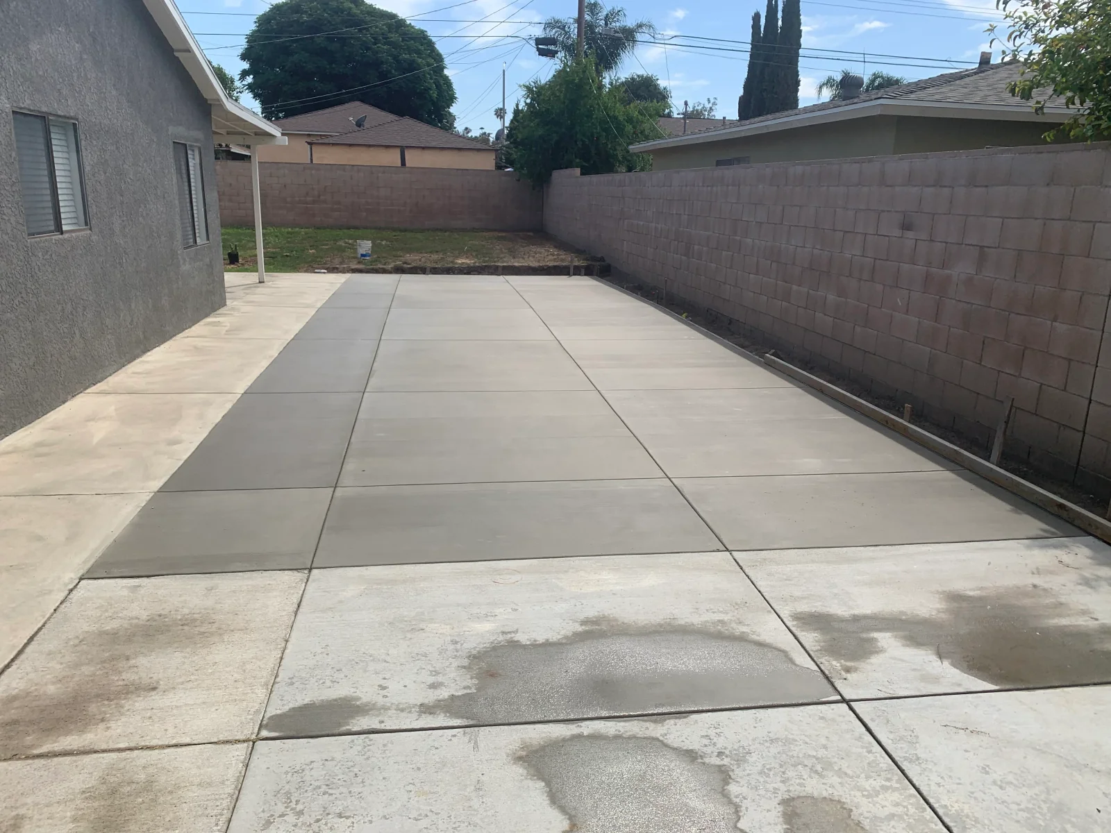 New concrete driveway with saw-cut control joints beside a stucco house and block wall