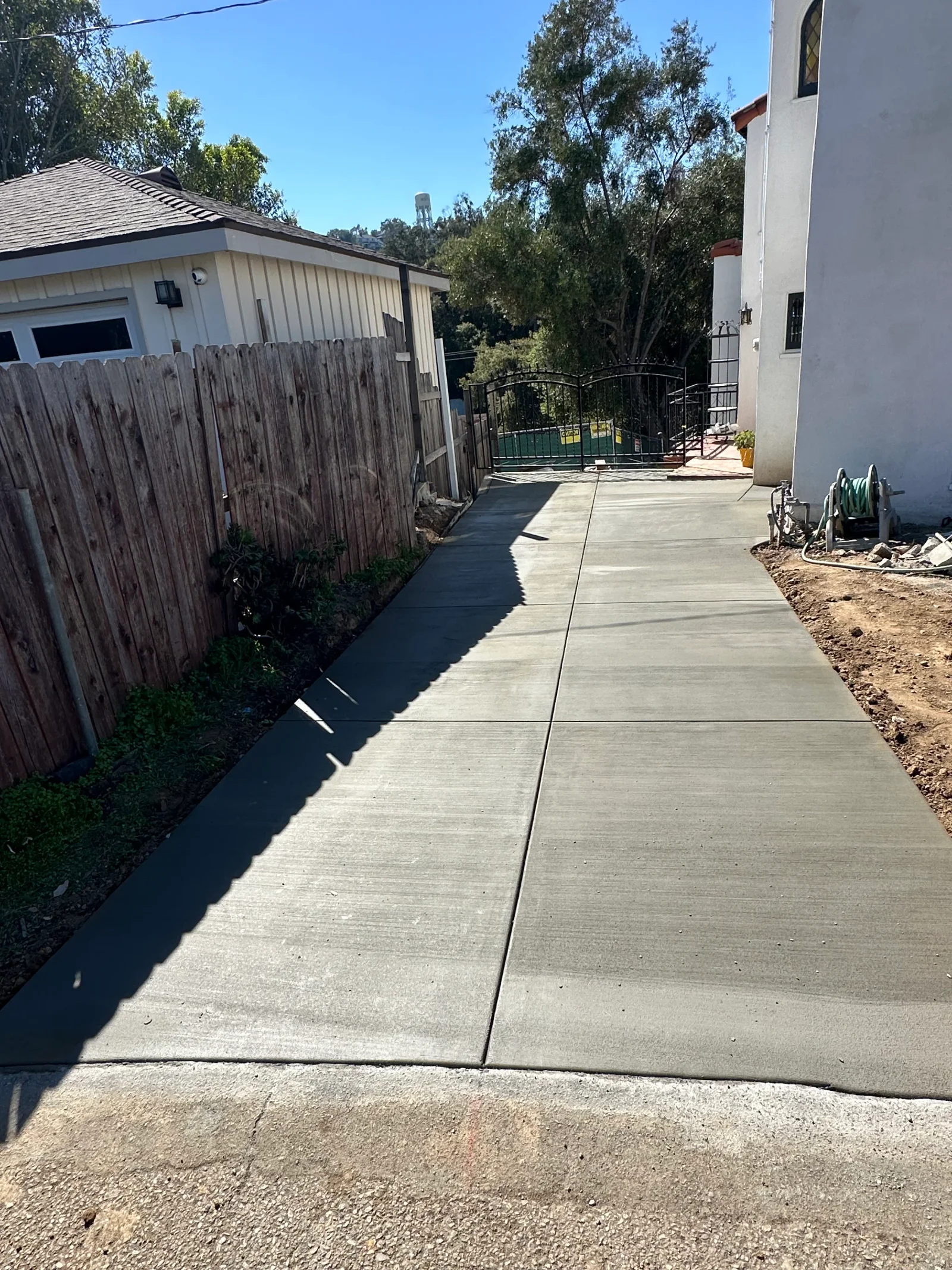 Freshly poured concrete side driveway with saw-cut control joints and broom-finished surface beside a wood fence