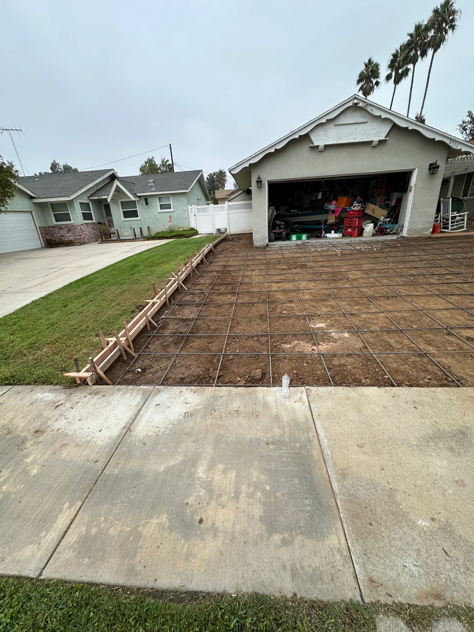 Wire mesh reinforcement and wood form boards staked over excavated soil for a driveway extension beside an attached garage