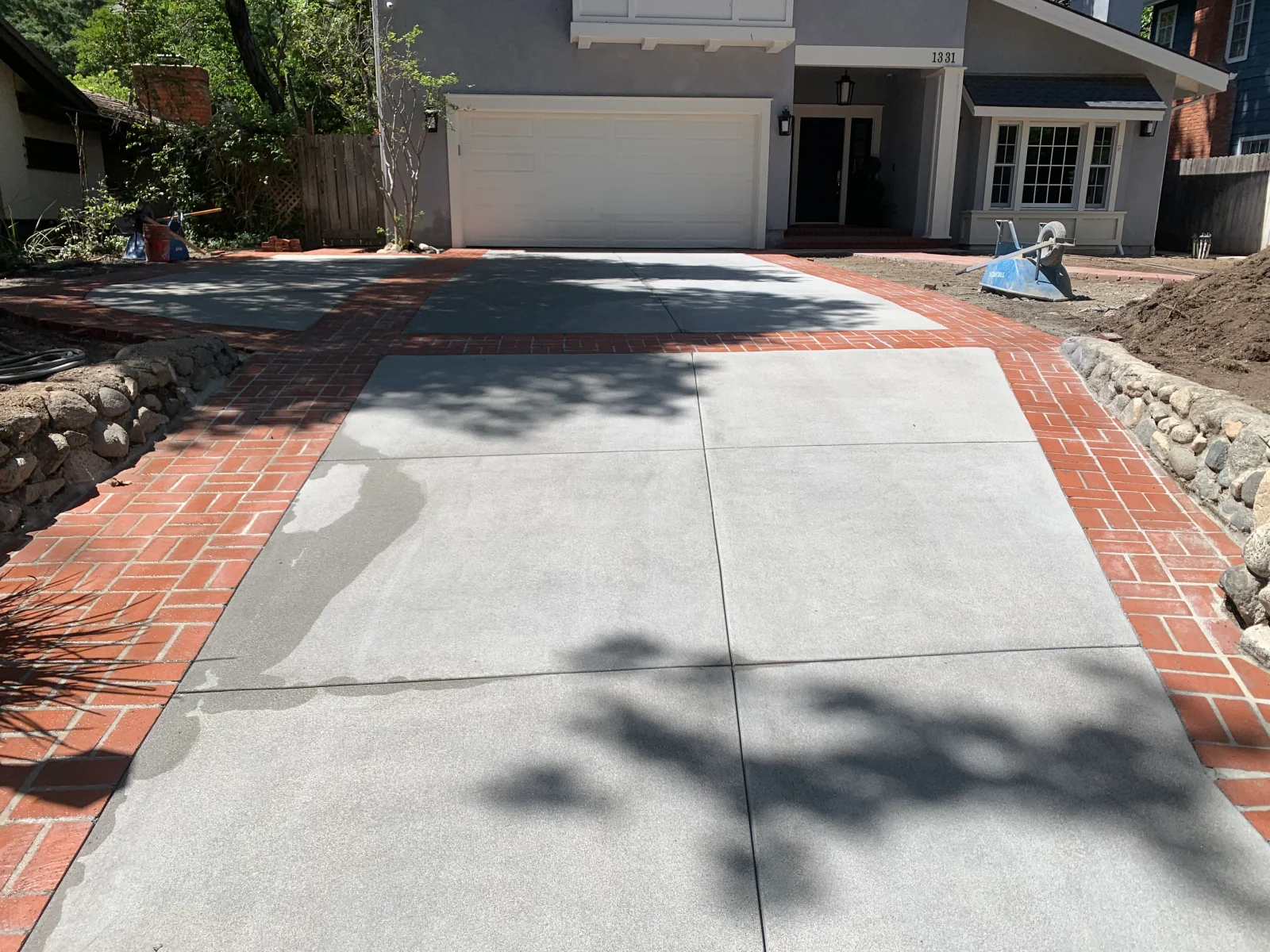 New concrete driveway with saw-cut joints framed by herringbone red brick border and river rock edging