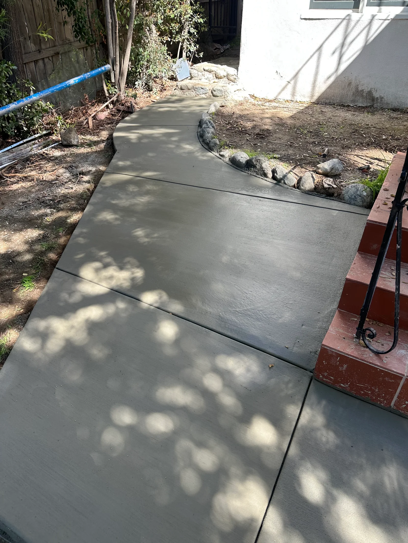 Smooth finished concrete walkway with control joints curving beside river rock border and red brick steps