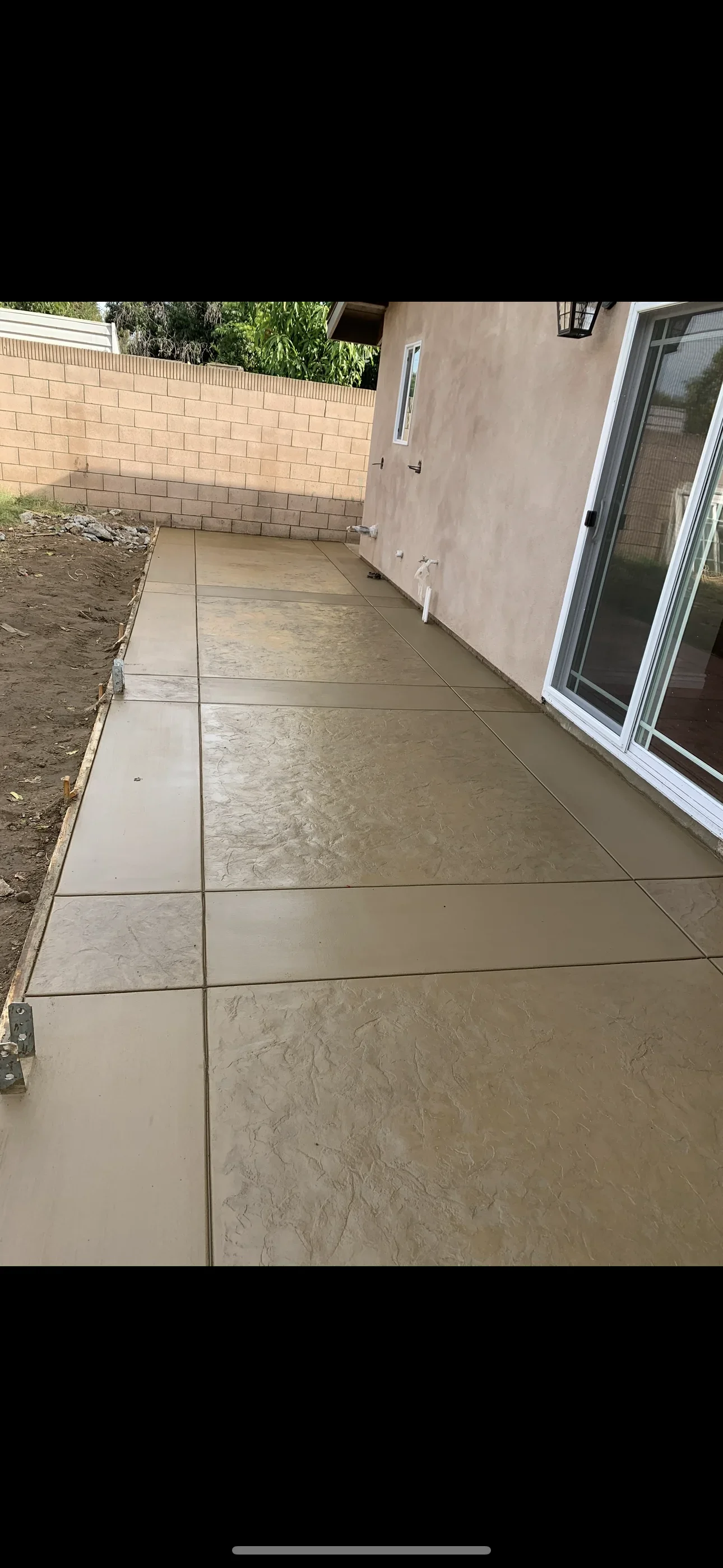 Textured tan stamped concrete patio with saw-cut joints beside stucco home and sliding glass door