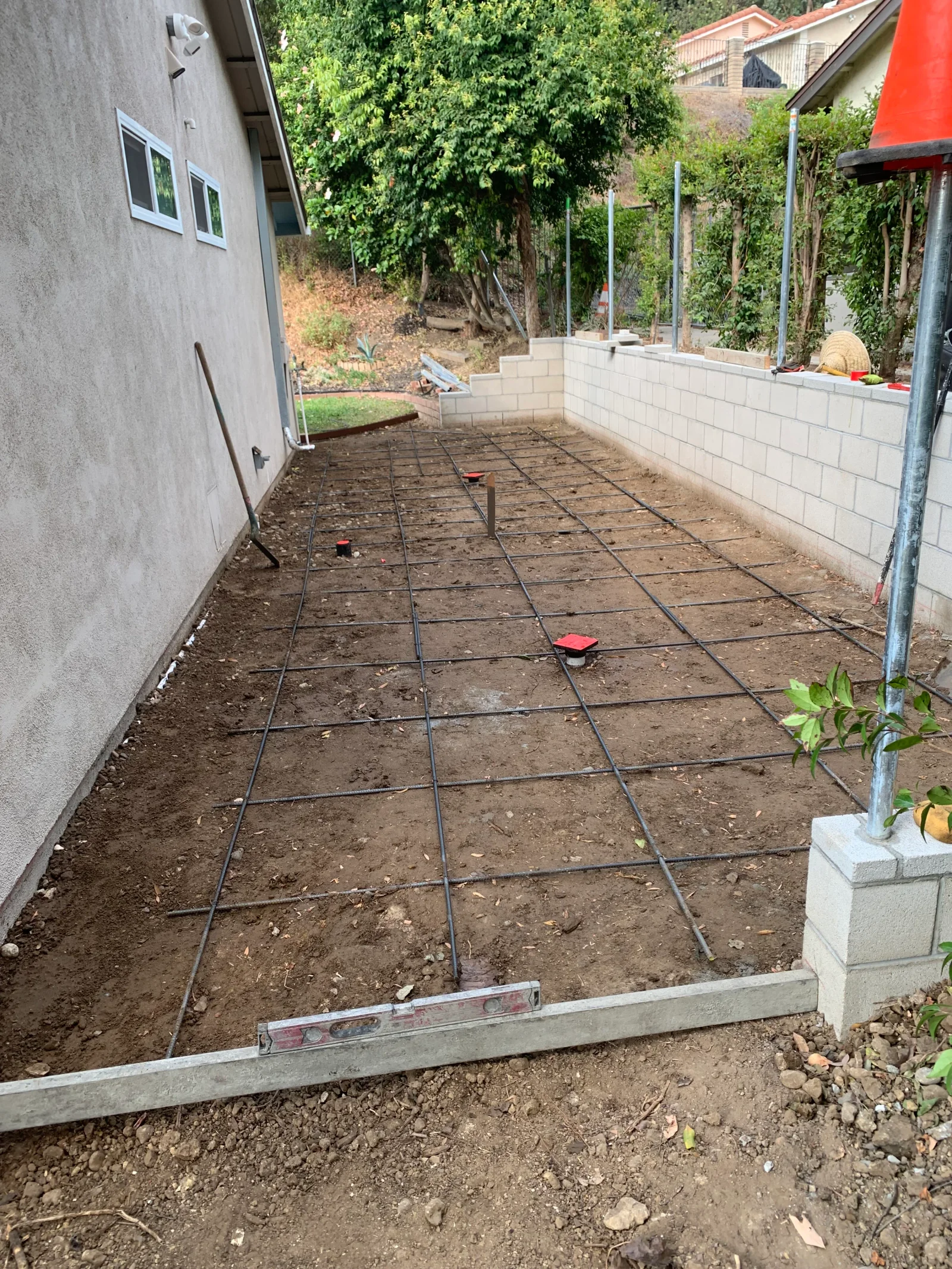 Steel rebar grid laid over soil inside concrete forms, with red rebar chairs and a level on the form board